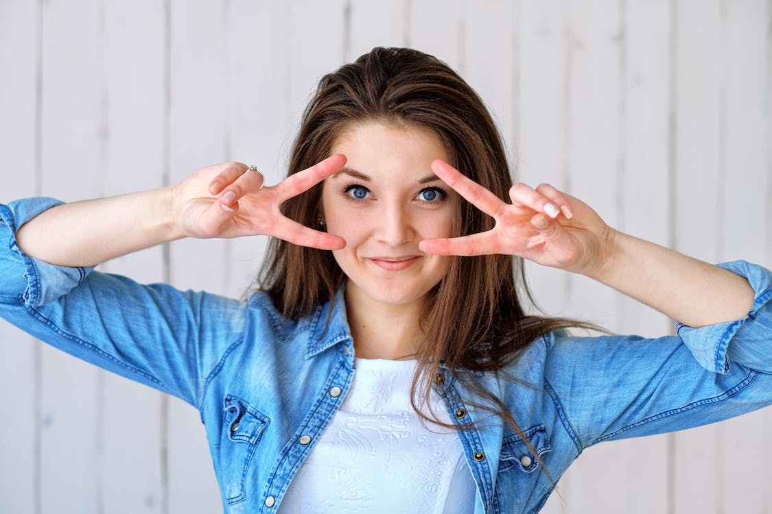 A Woman with Flawless Facial Skin After RejuvenationTherapy Making a Horizontal Peace Sign with Both Hands